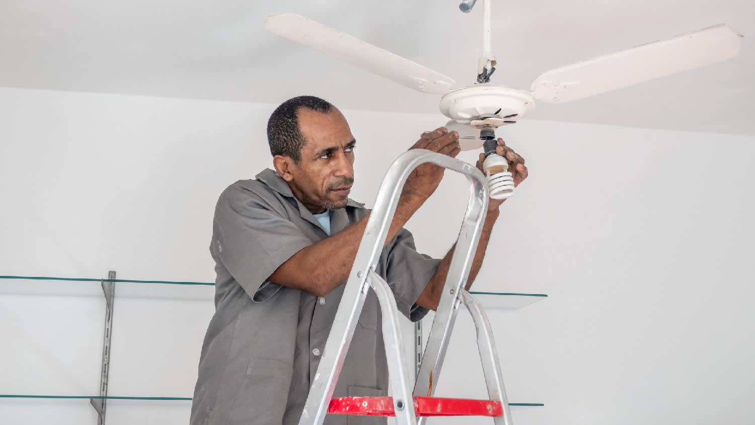 An electrician changing the light bulb in a ceiling fan