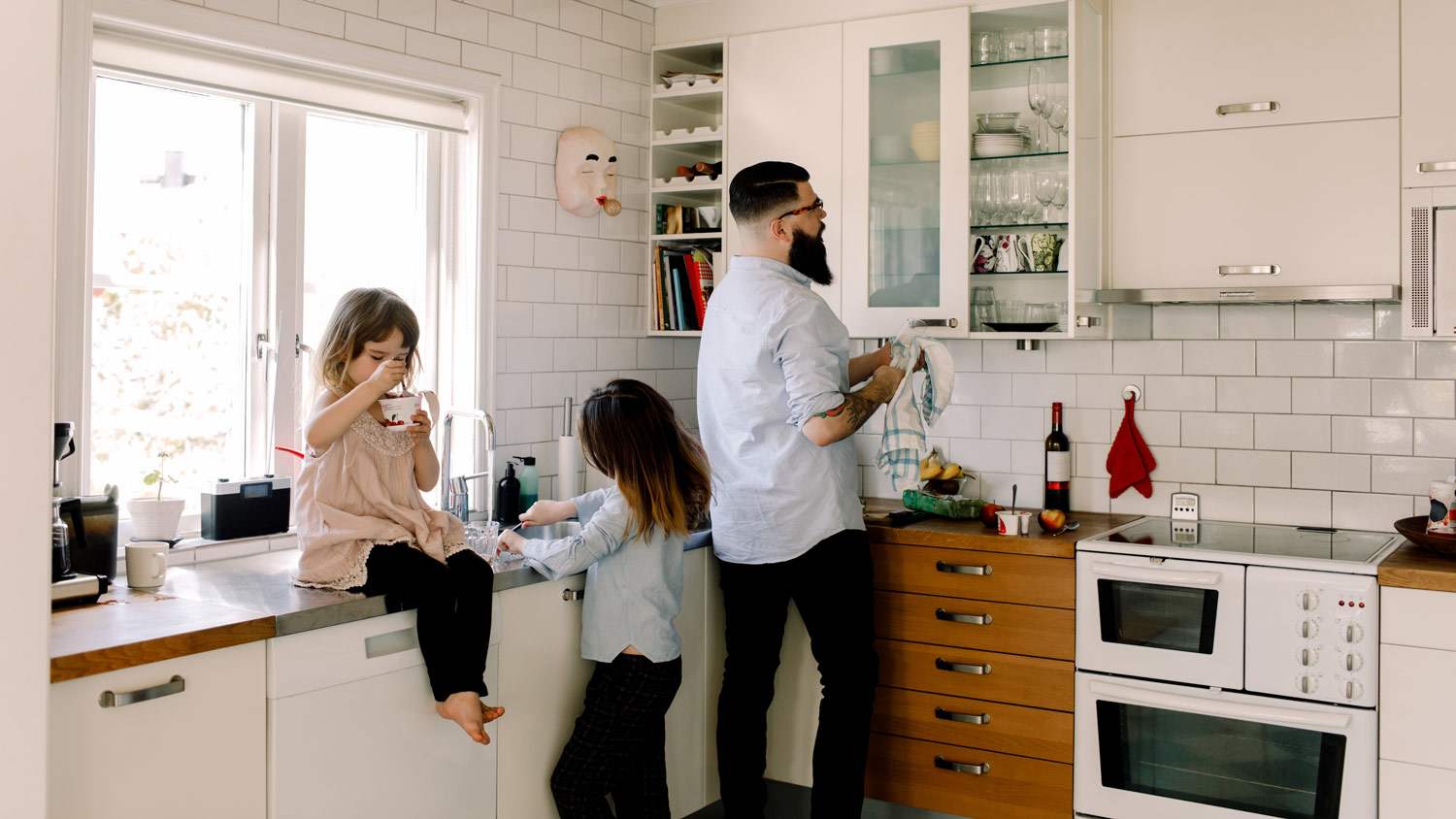 Father and daughter do chores while other daughter is having a snack