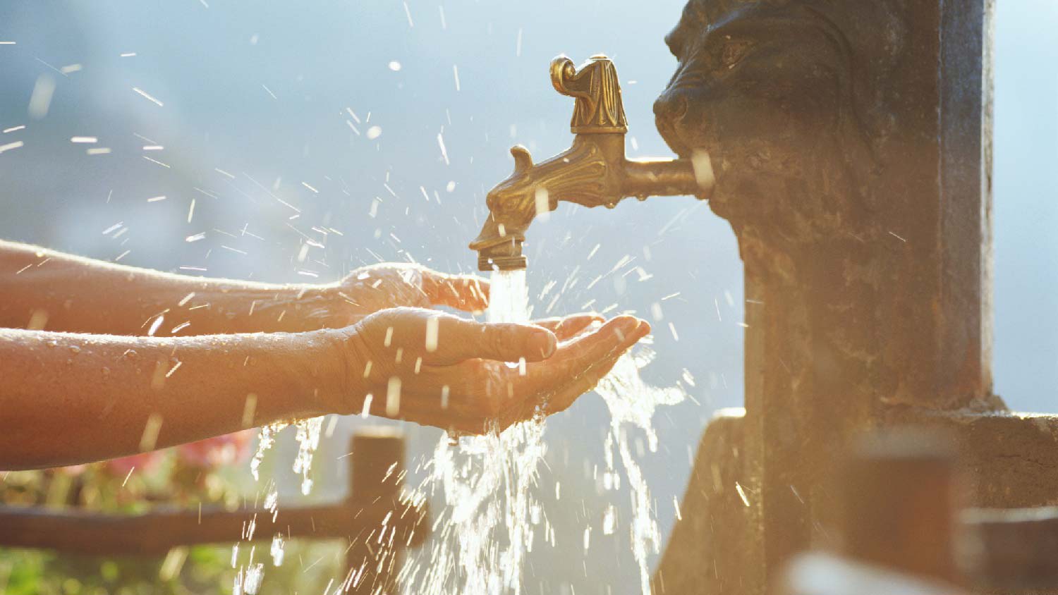 A person washing hands in an outdoor spigot