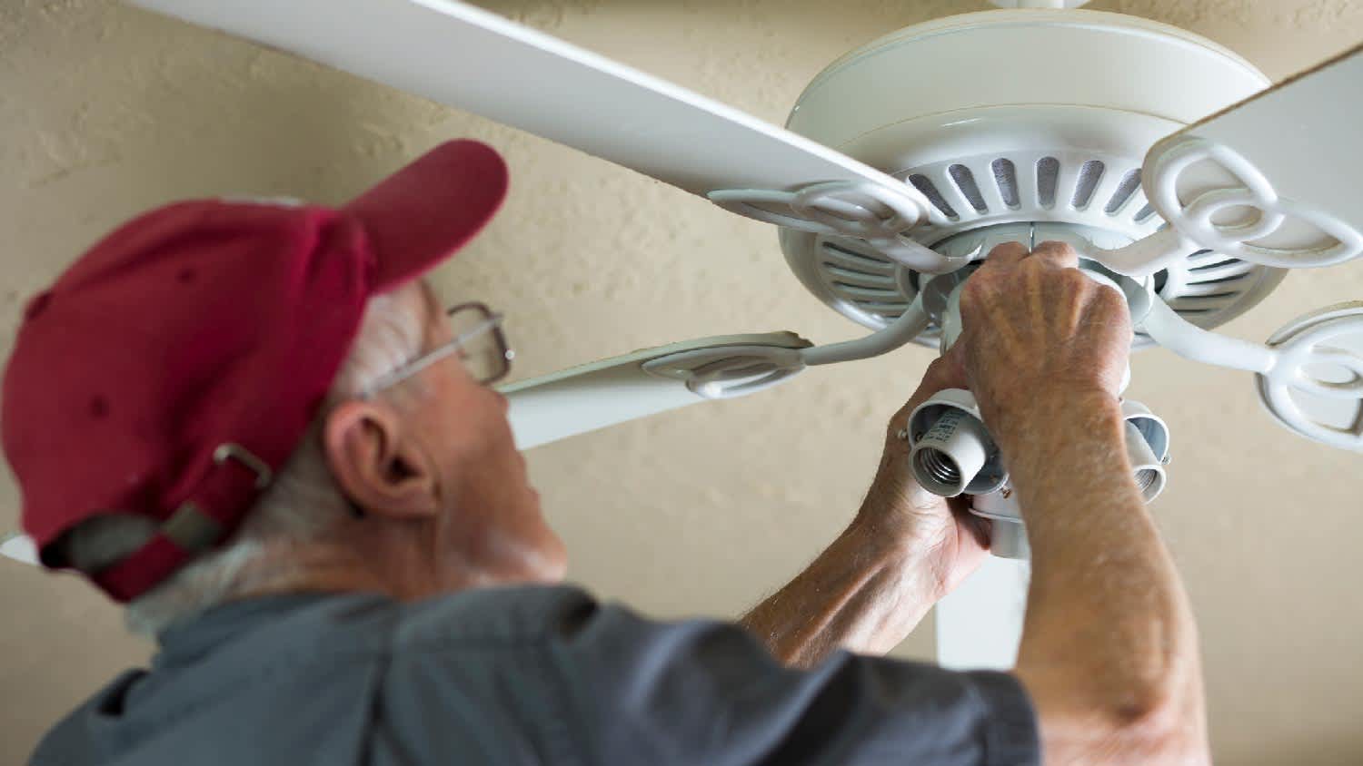 A man adjusting a ceiling fan’s direction