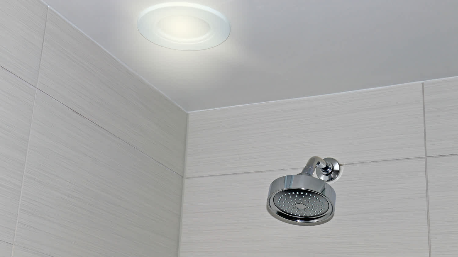 Shower head on a bathroom ceramic tile wall and circular light fixture on the ceiling