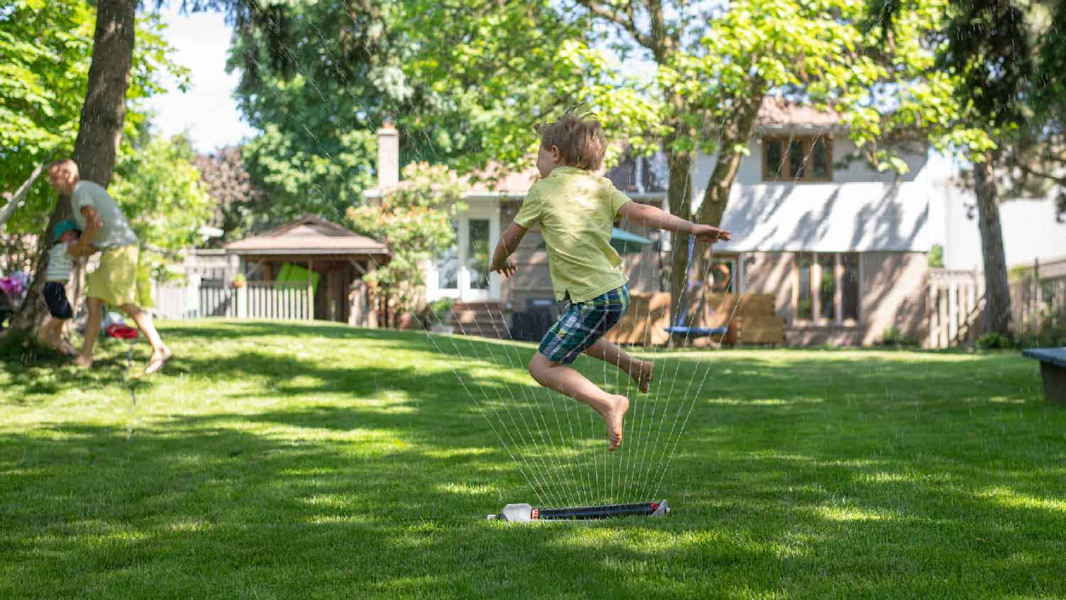 A boy playing in the backyard with the sprinklers