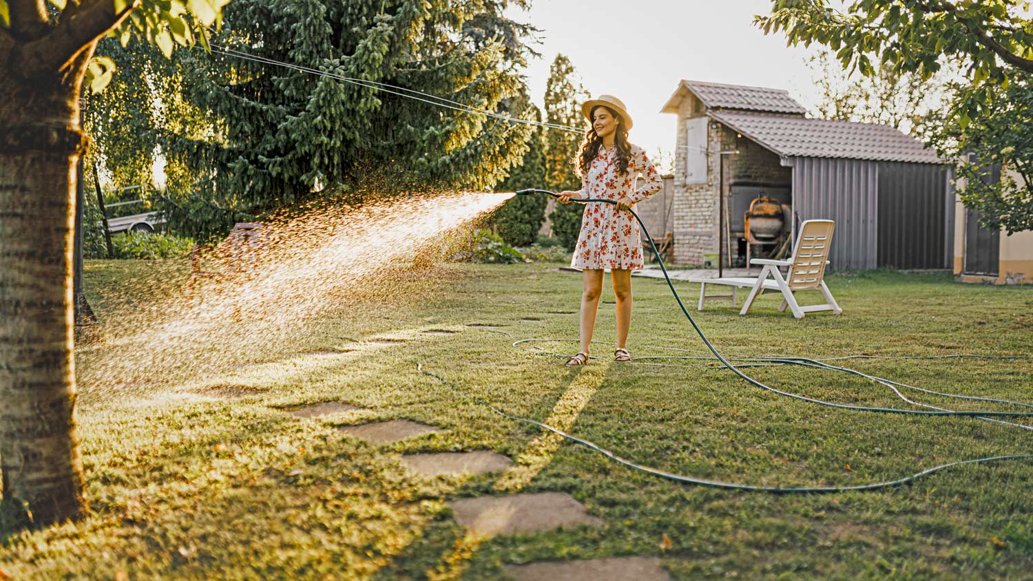 woman watering plants with a garden hose in backyard