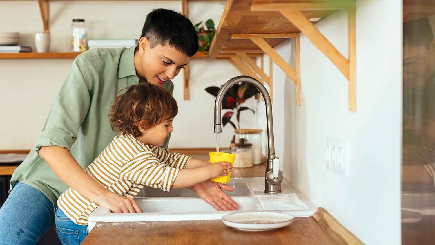 Mother helping son filling cup with tap water