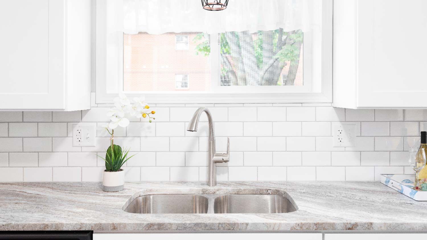 A kitchen sink beneath a window and a marble countertop