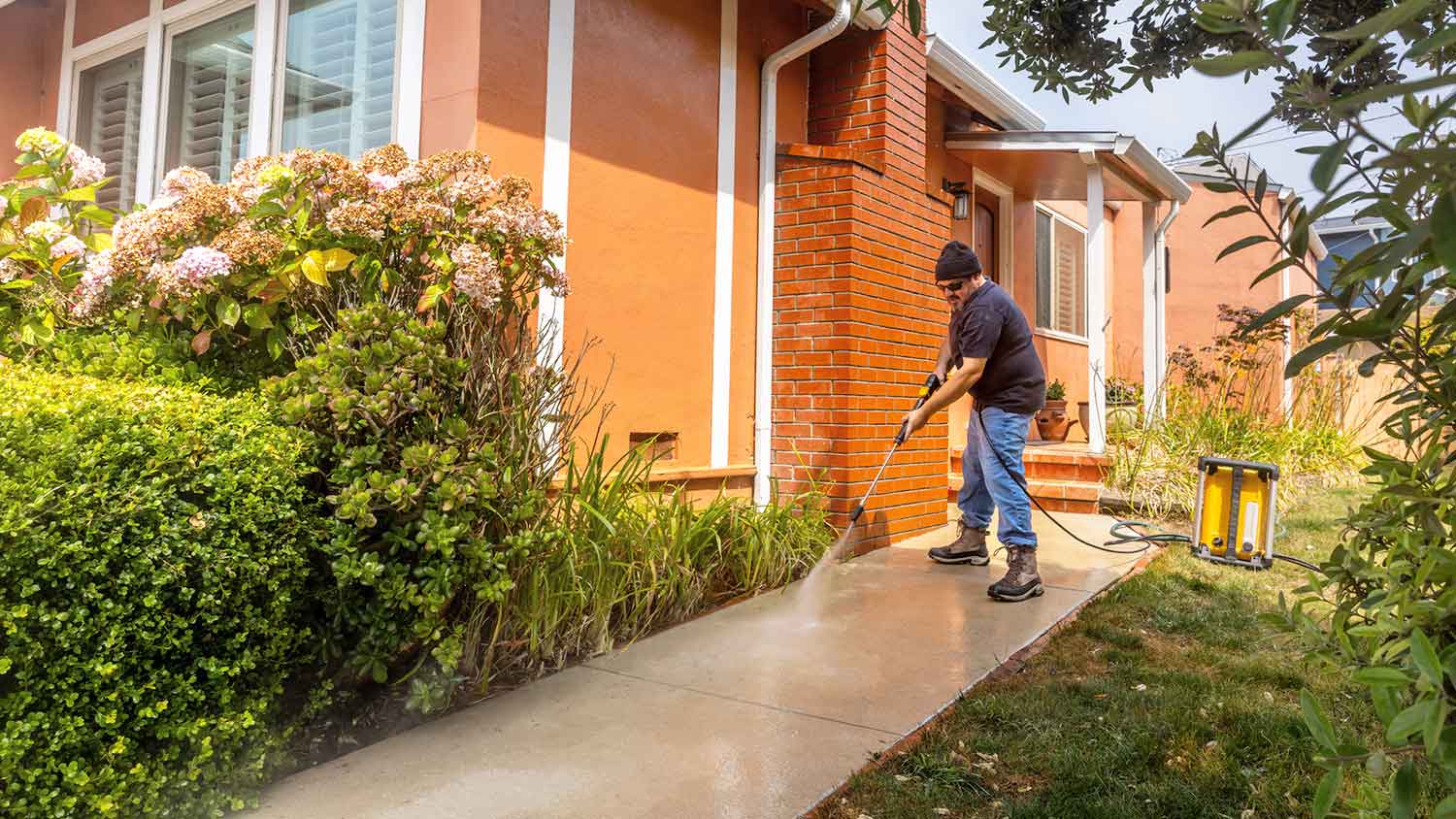 Man using pressure washer to wash concrete walkway