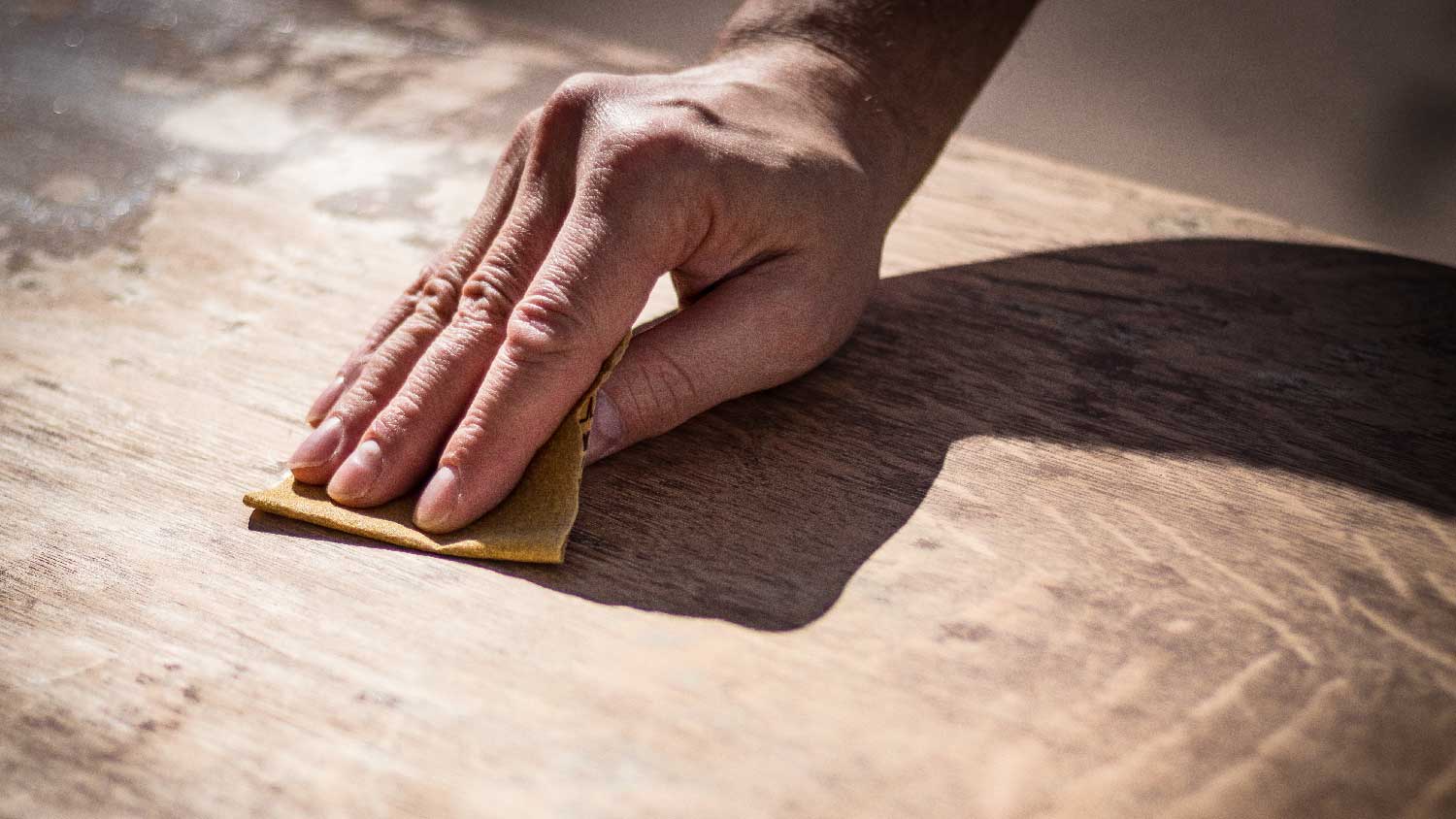 A man sanding a wooden cabinet with a fine grit sanding pad