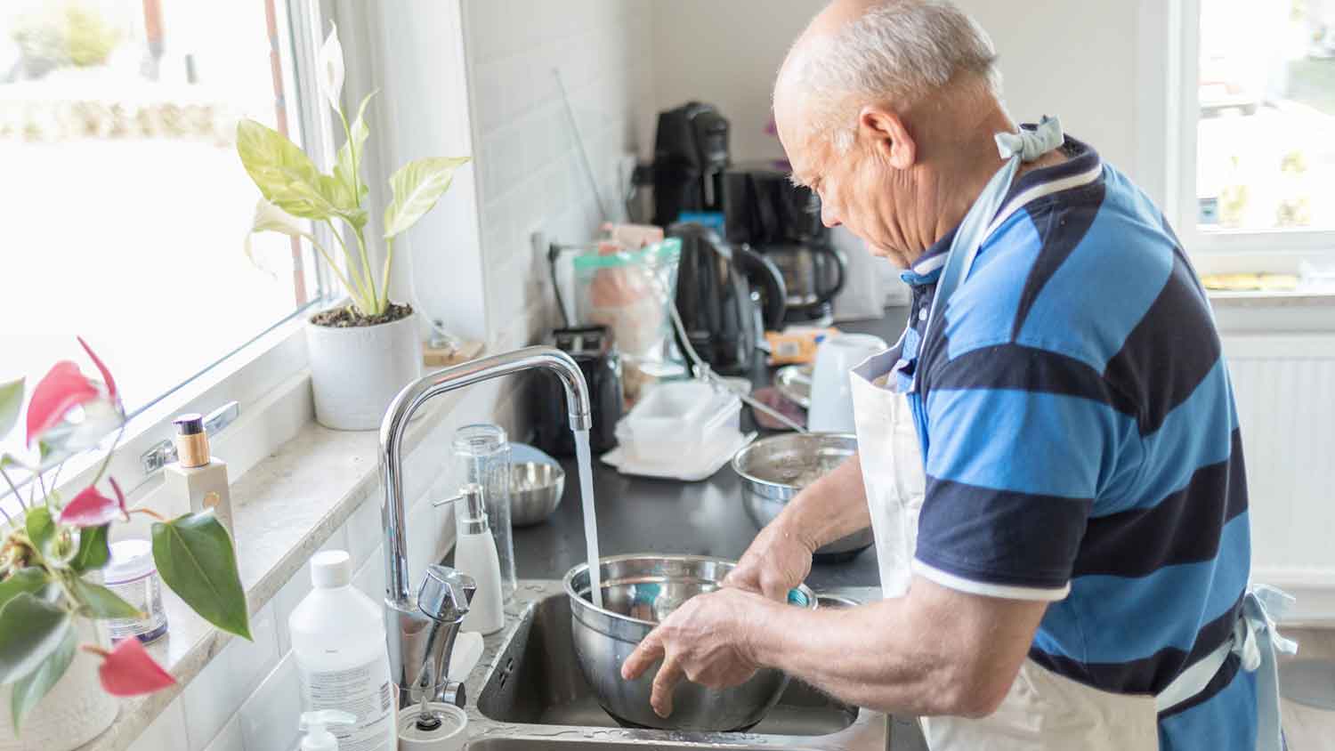 Senior man washing dishes in the kitchen sink