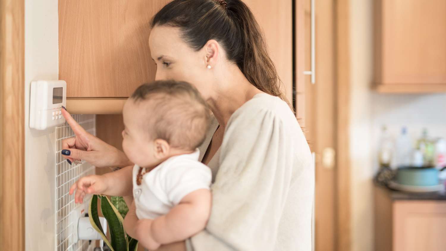 Young Mother holds her baby boy on her arms and shows him how to adjusts the temperature