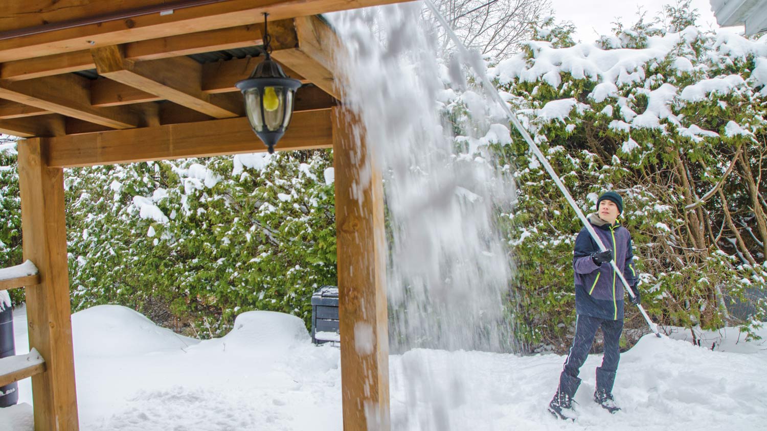 Teenage boy removing snow from patio roof