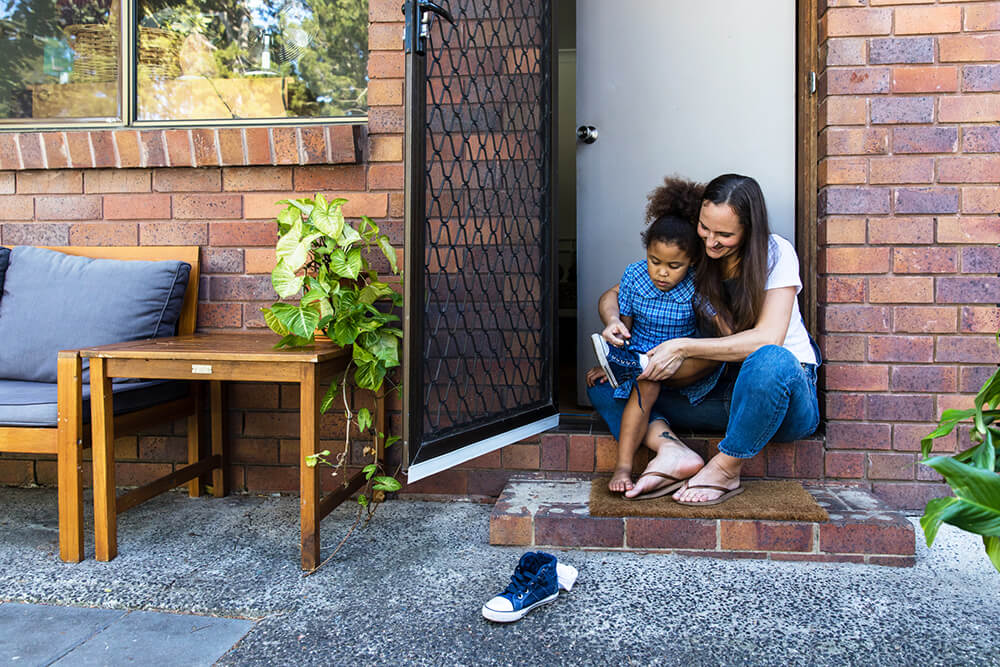 Woman helping child put on shoes with an open screen door