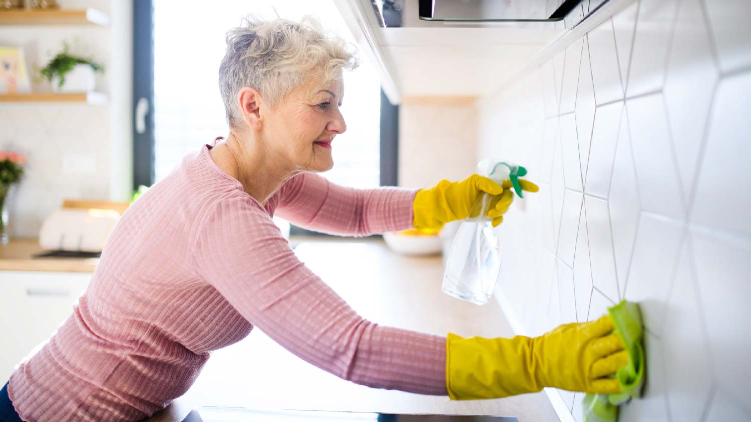 A senior woman spraying vinegar solution to clean tiles