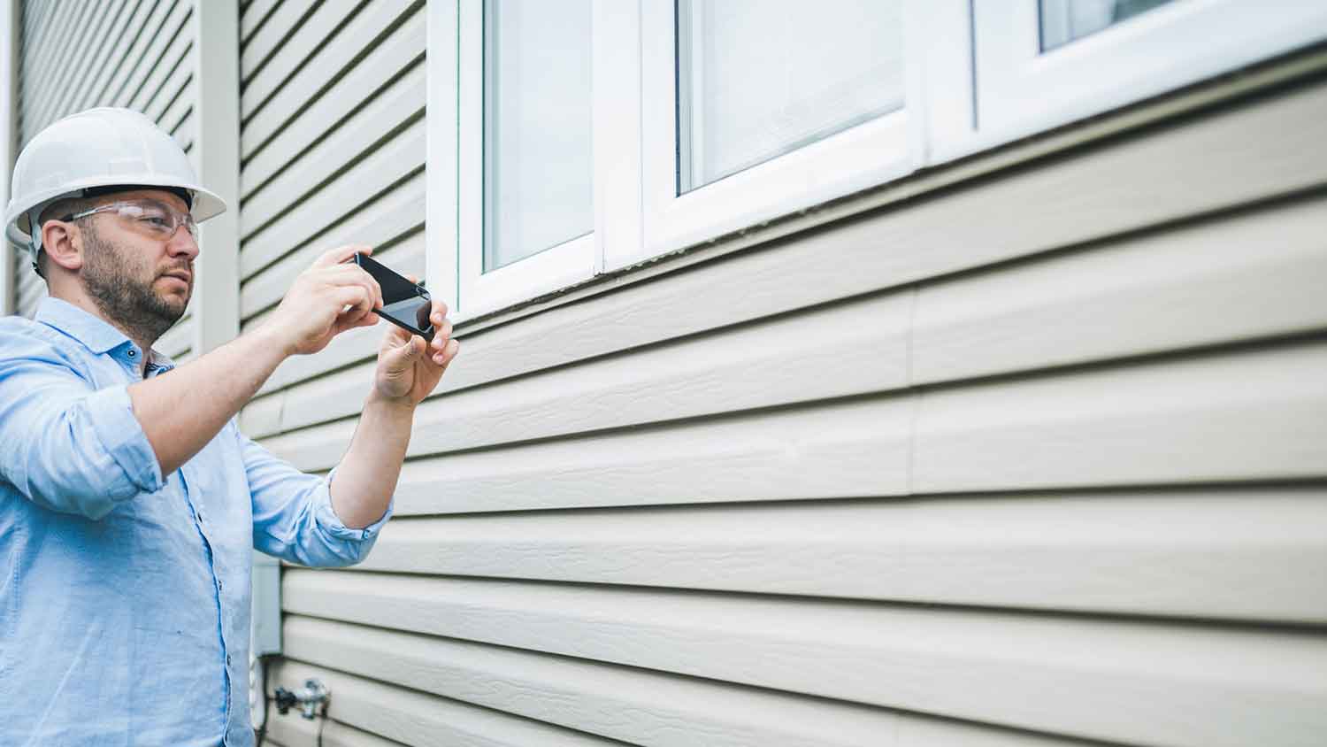 Inspector using his phone to take pictures of the house siding
