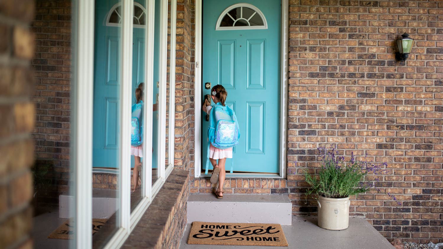 A young girl with backpack opening her house’s front door