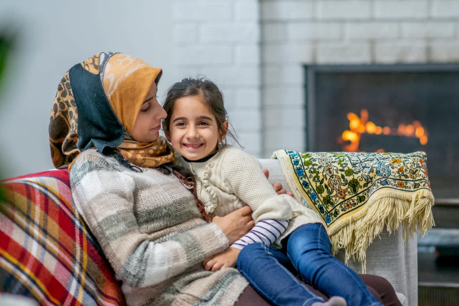 A Muslim mother is sitting on the couch with her daughter