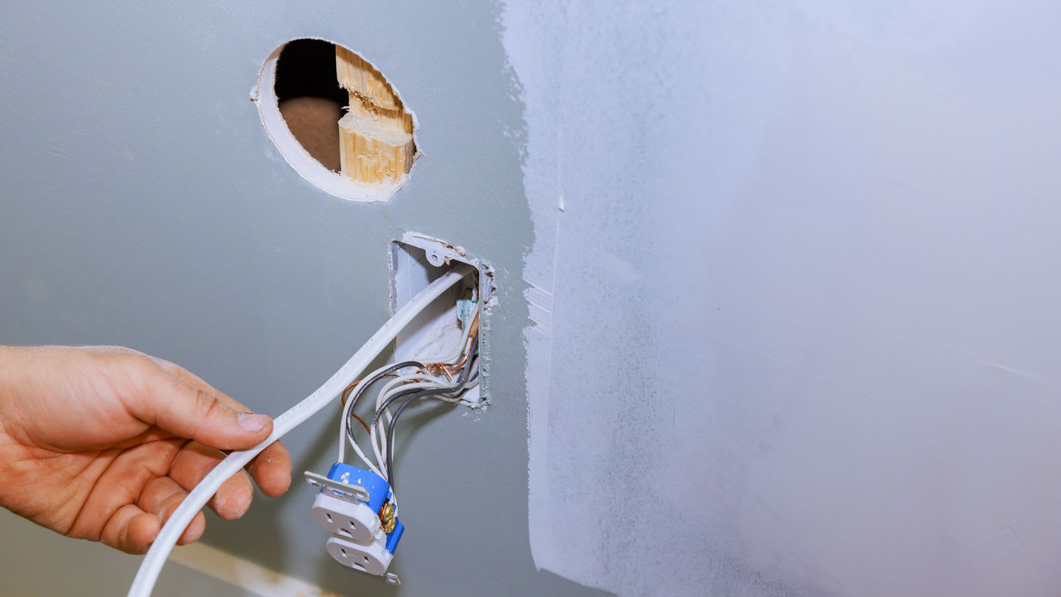 man holding wires through wall