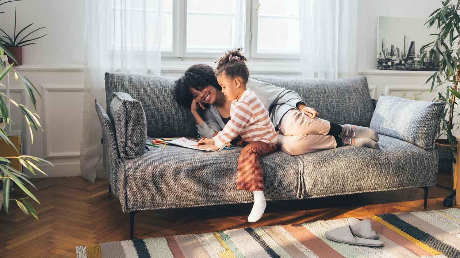 Mother lying on the couch watching daughter drawing
