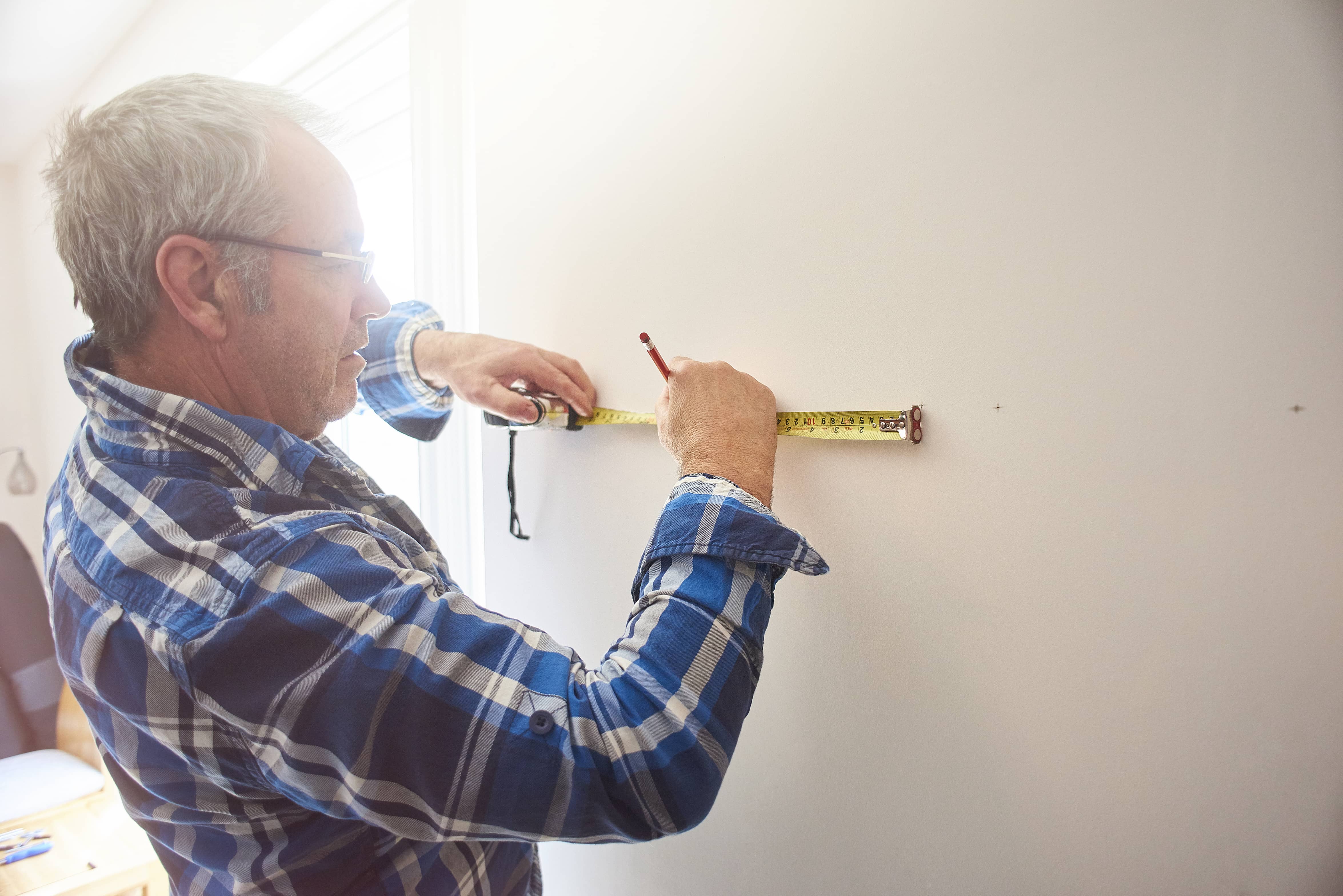 man measures the wall near his window to find the wall studs