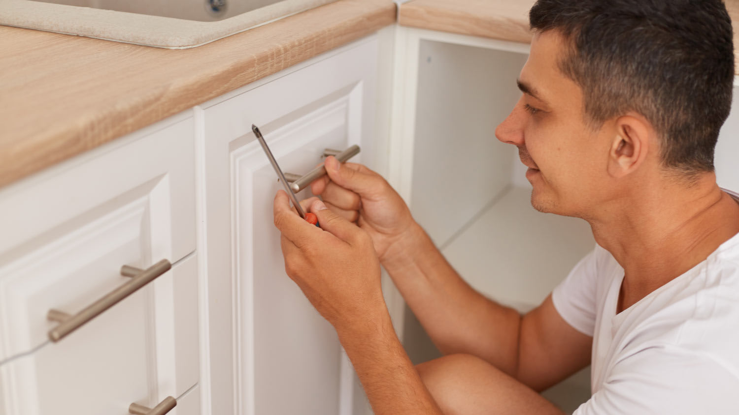 man installing new hardware on white kitchen cabinet