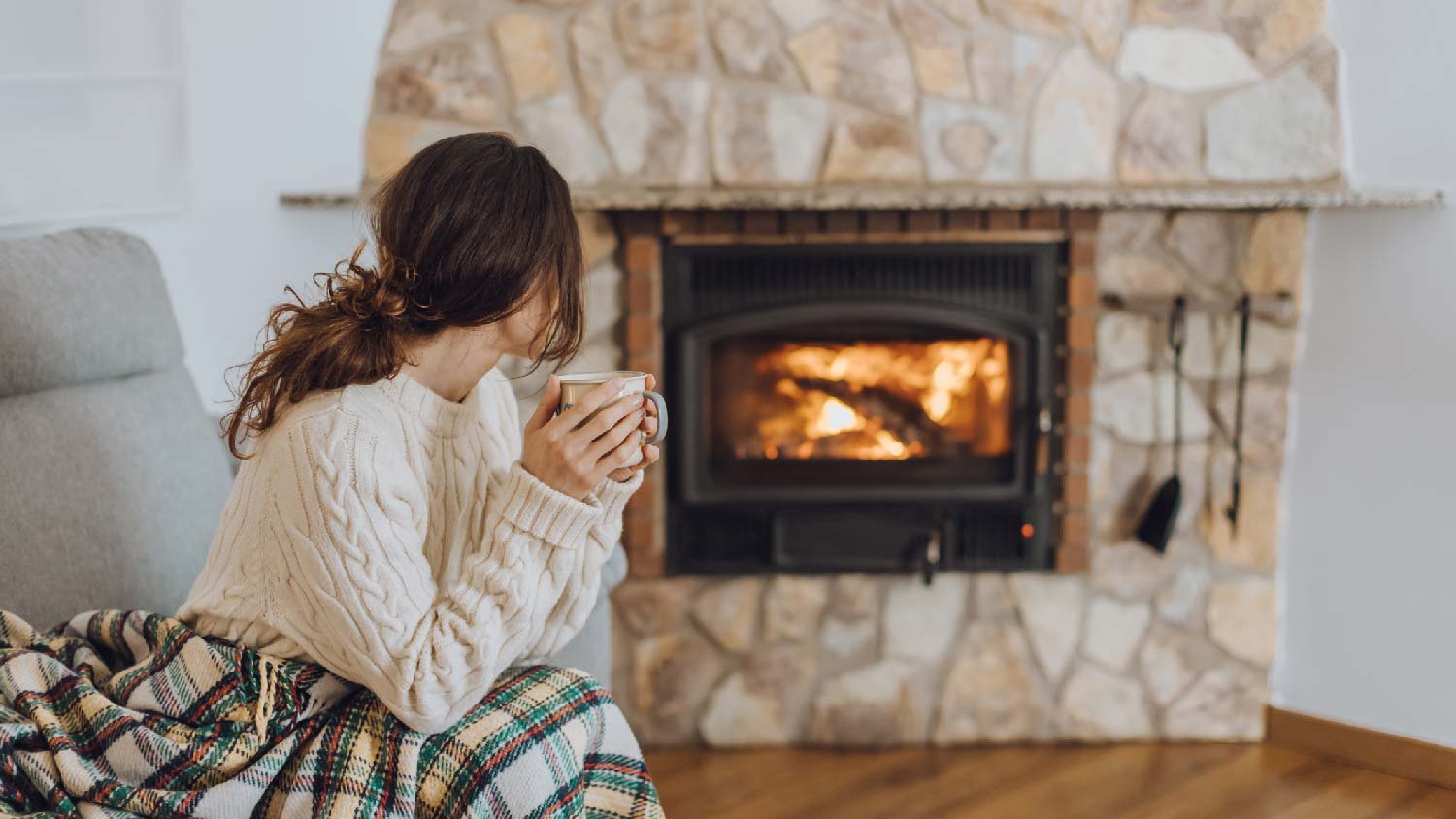 A woman enjoying her beverage in front of the fireplace