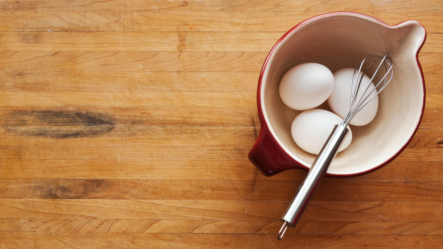 Bowl filled with eggs and whisk on butcher block counter