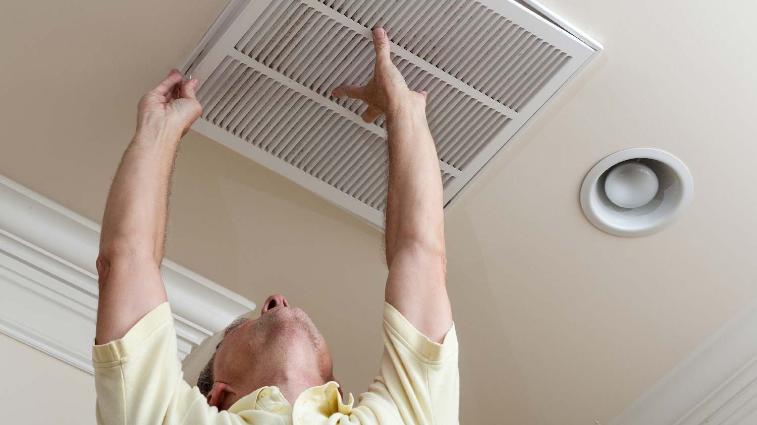 A man opening a ceiling air vent