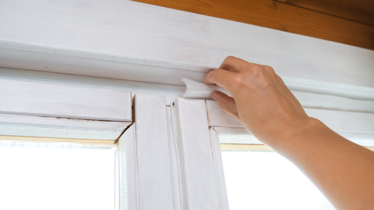 A woman’s hand sealing a window with window tape