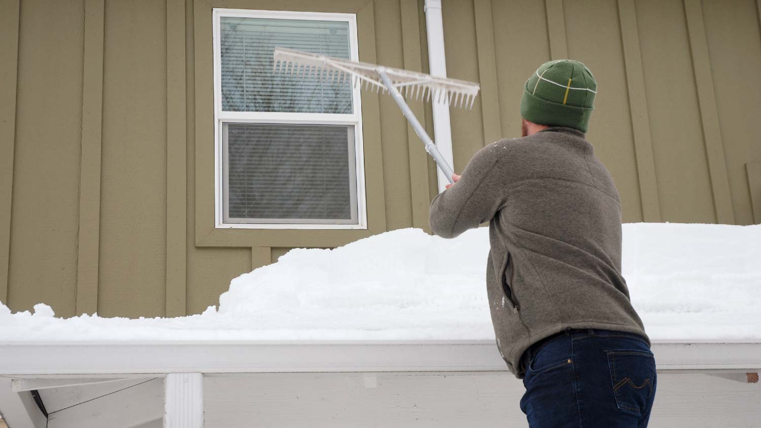 A person removing snow from roof with a rake