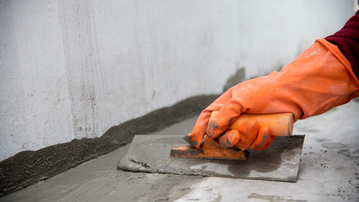 Close-up of a hand holding a trowel laying concrete slab