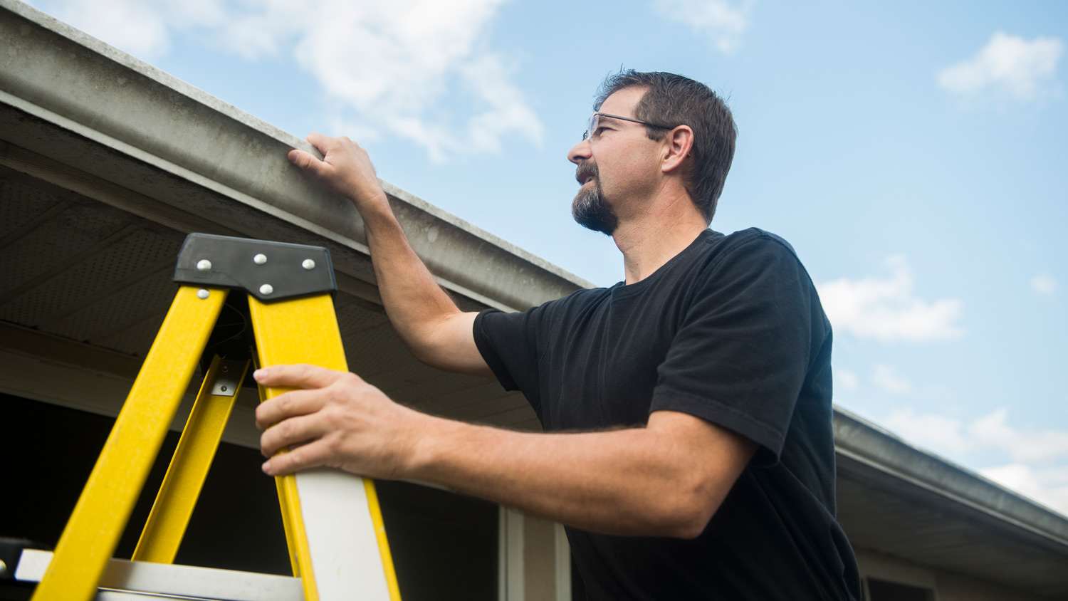 Man Inspects Roof Condition of House on a ladder