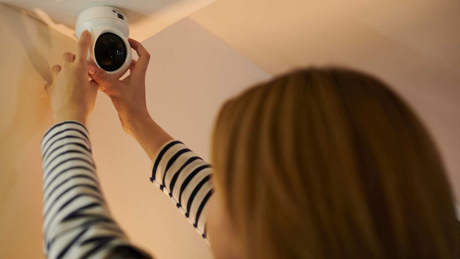 woman installing security camera on ceiling