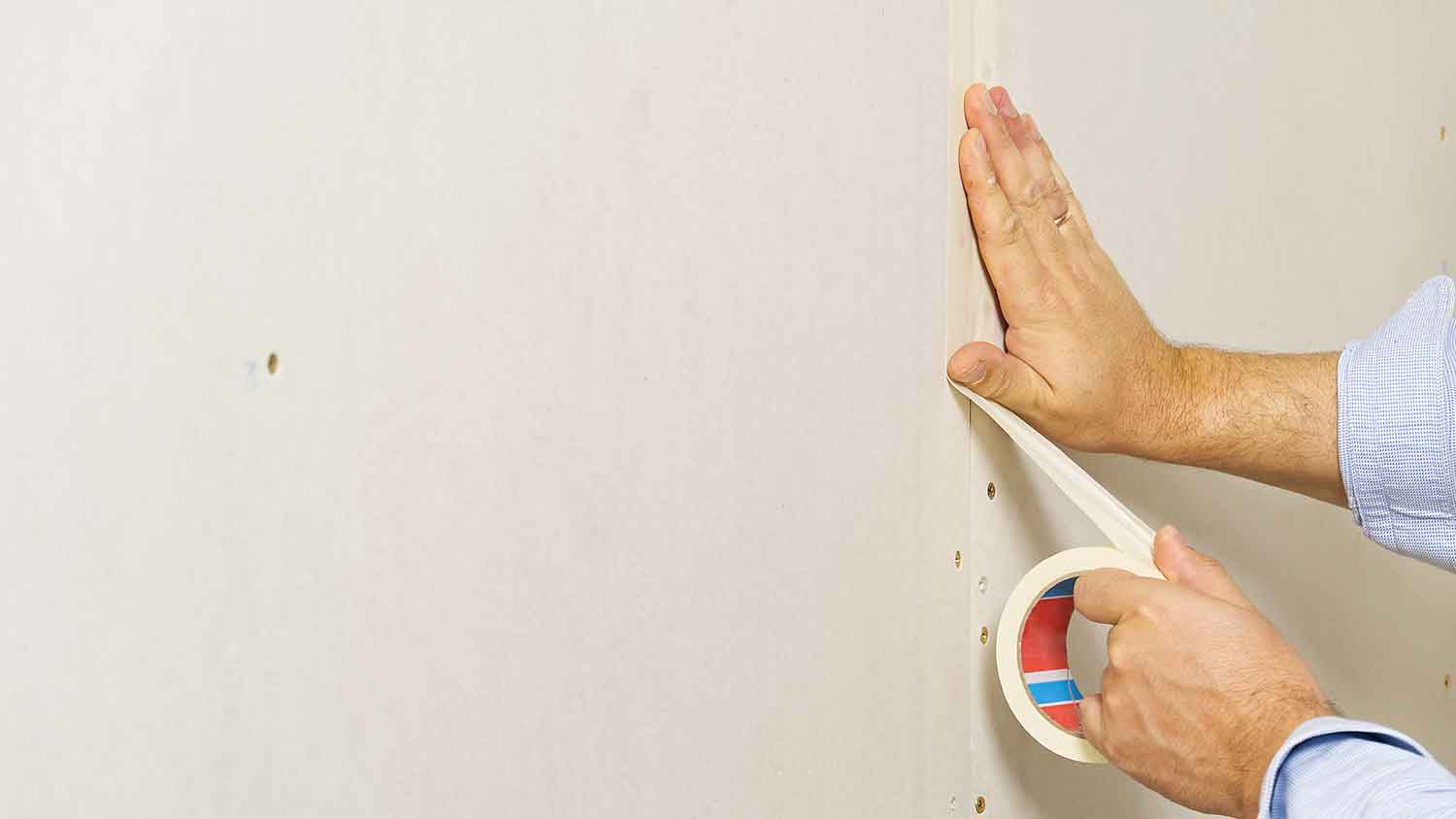 Worker applying paper drywall tape over the seams