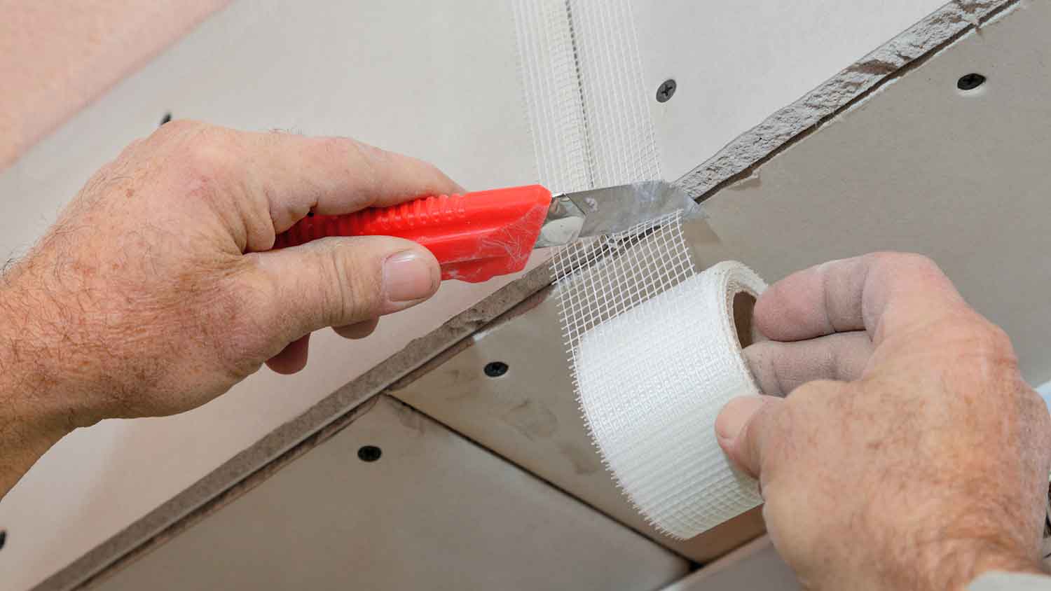 Worker using cutter to cut a piece of mesh drywall tape