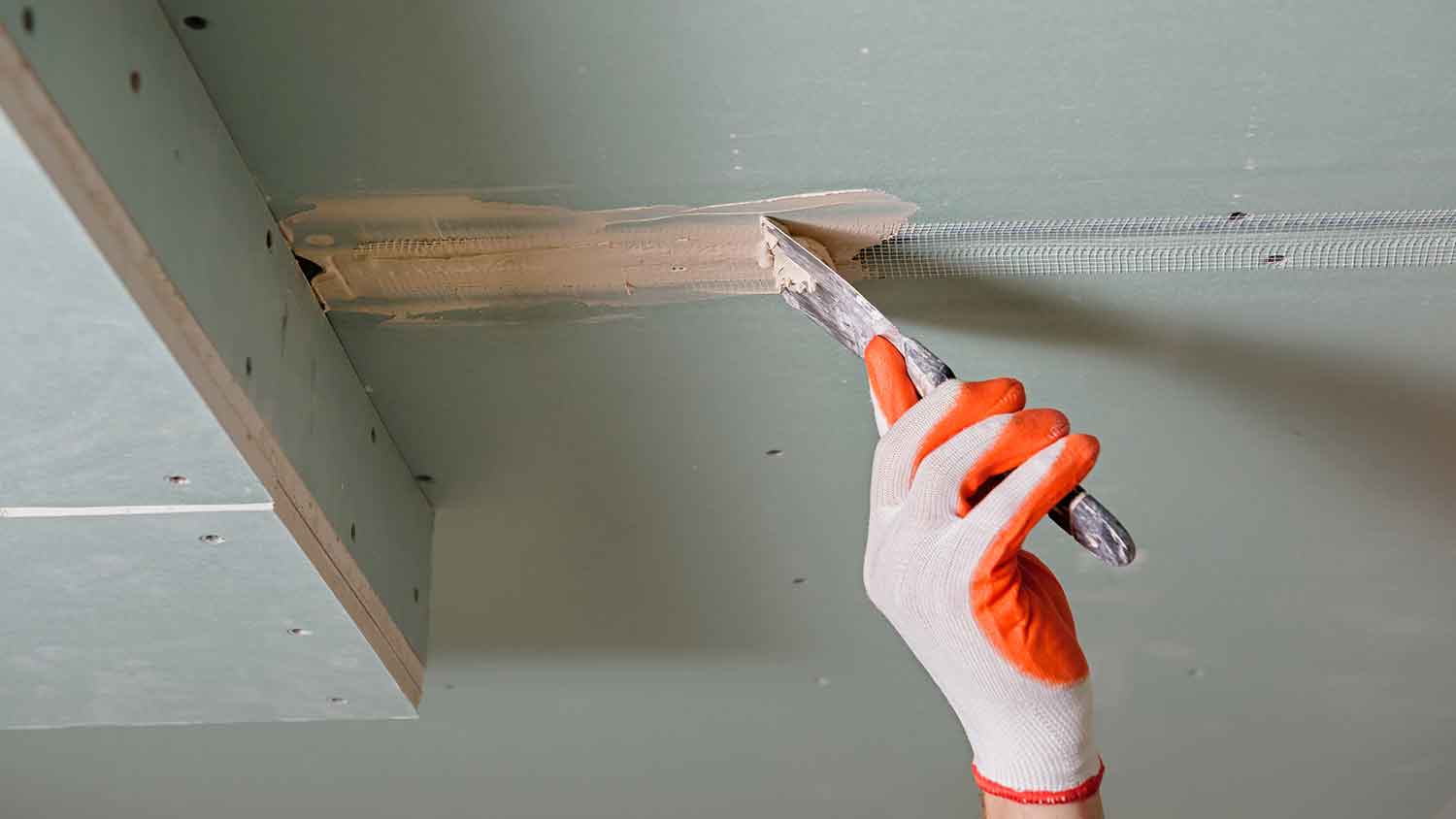 Worker applying drywall mud over mesh tape