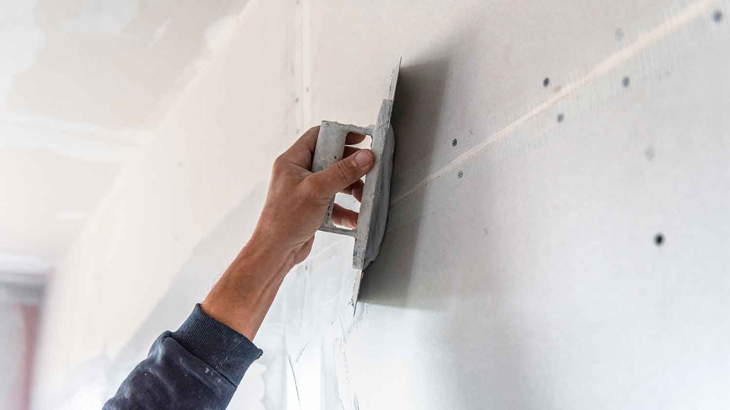 Worker taping and mudding new drywall