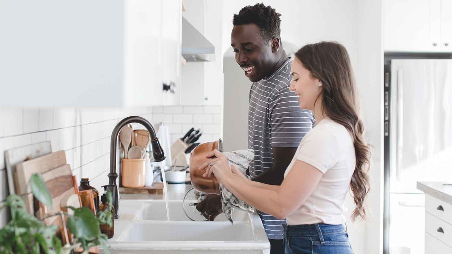 Couple in a bright kitchen washing dishes in the sink