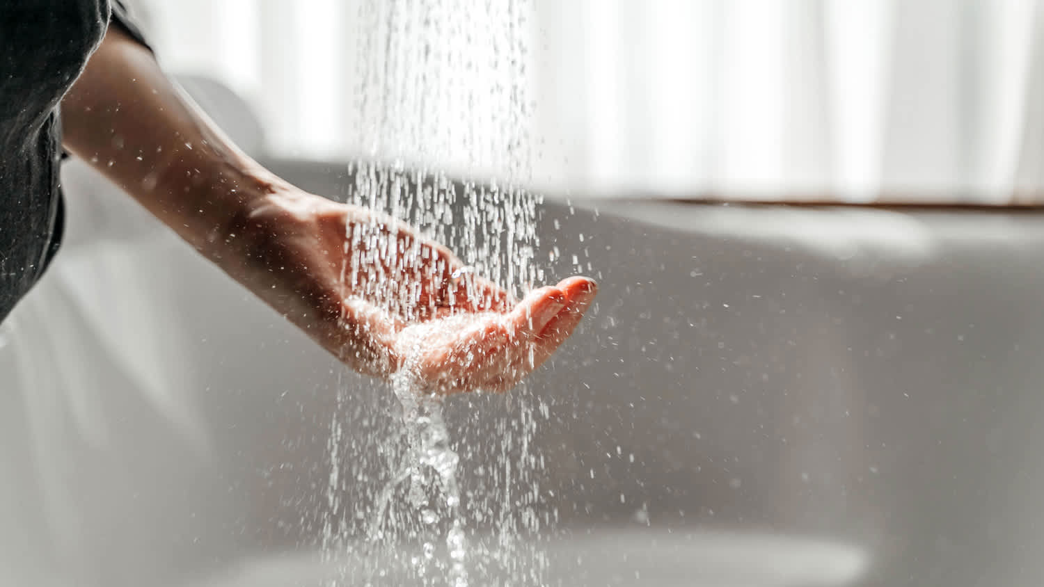 A woman's hand touches the water running from the shower