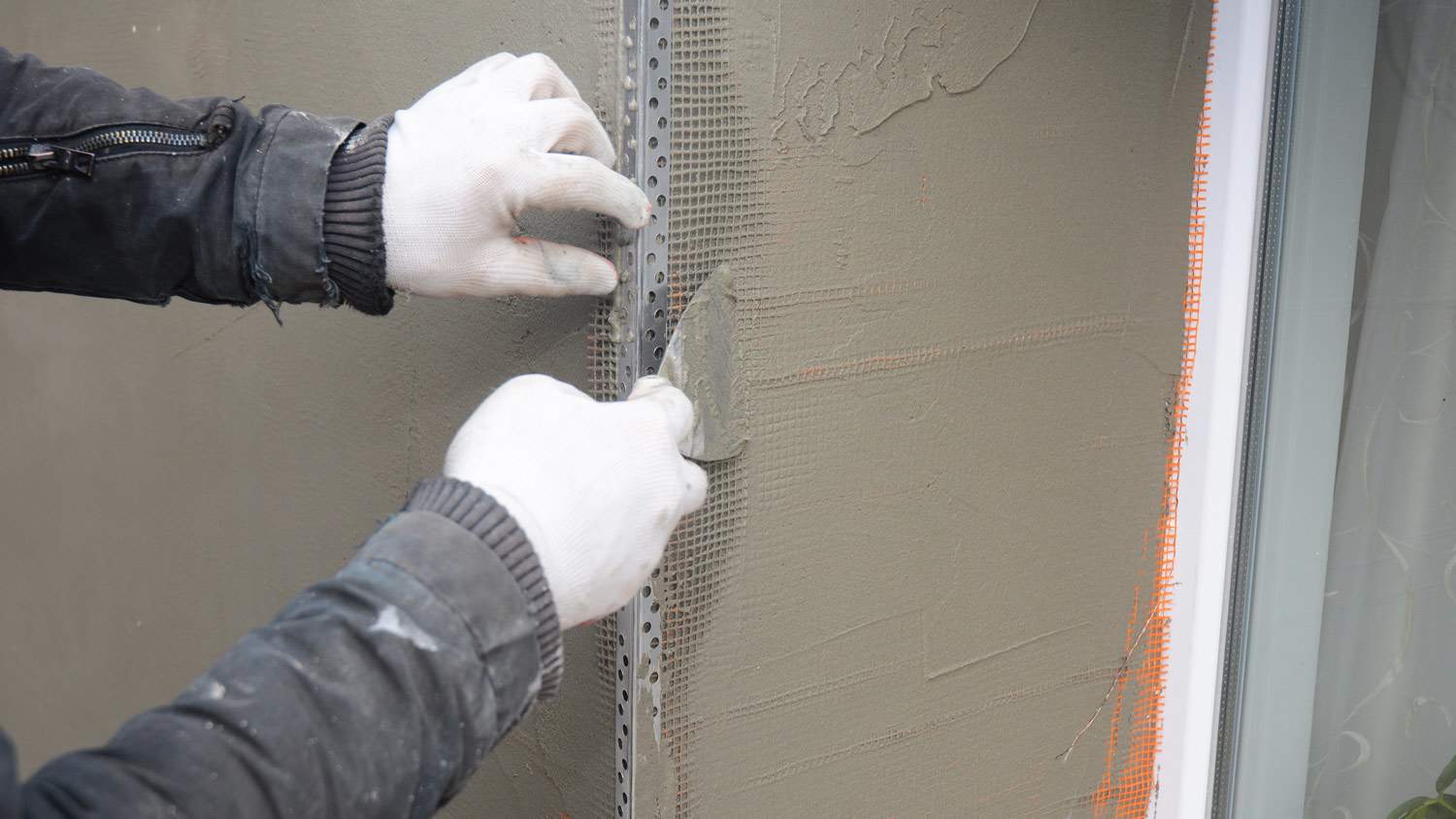 Contractor plastering wall with putty knife, fiberglass mesh, plaster mesh after rigid insulation