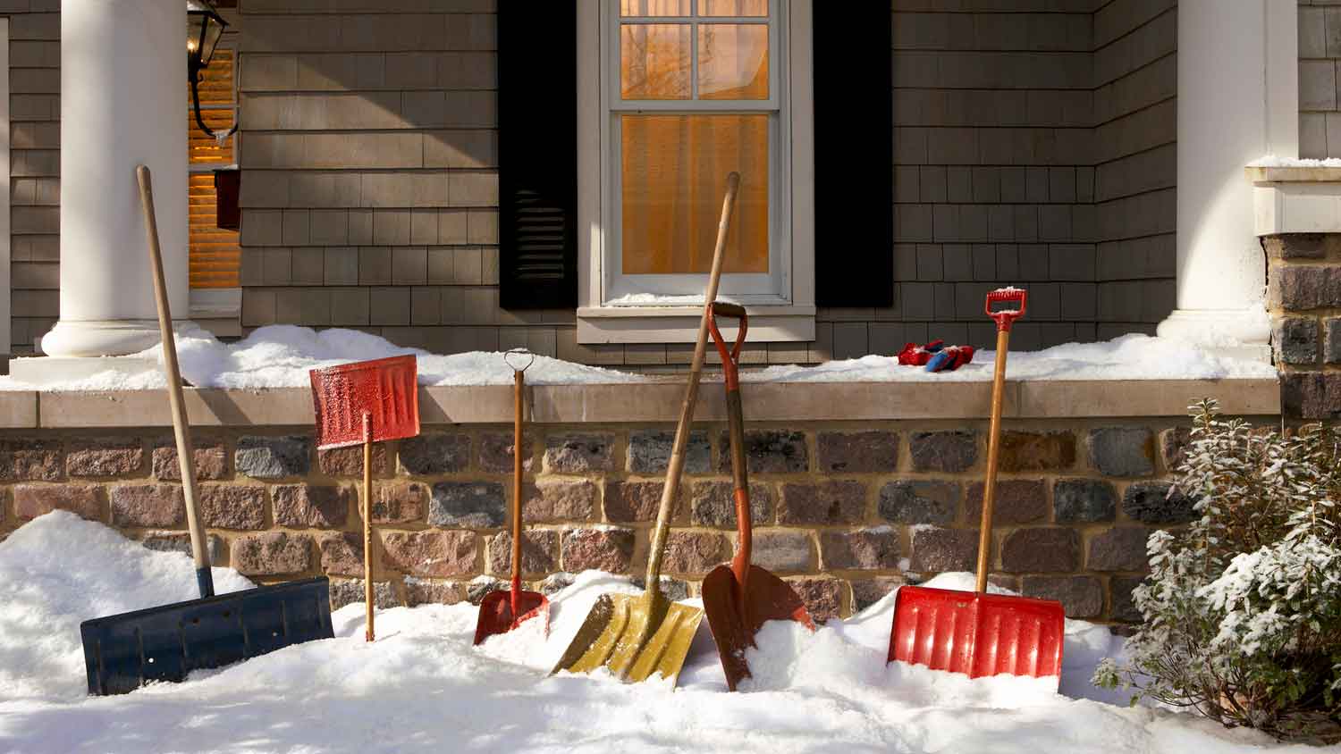 Snow shovels lined up against the side of a house