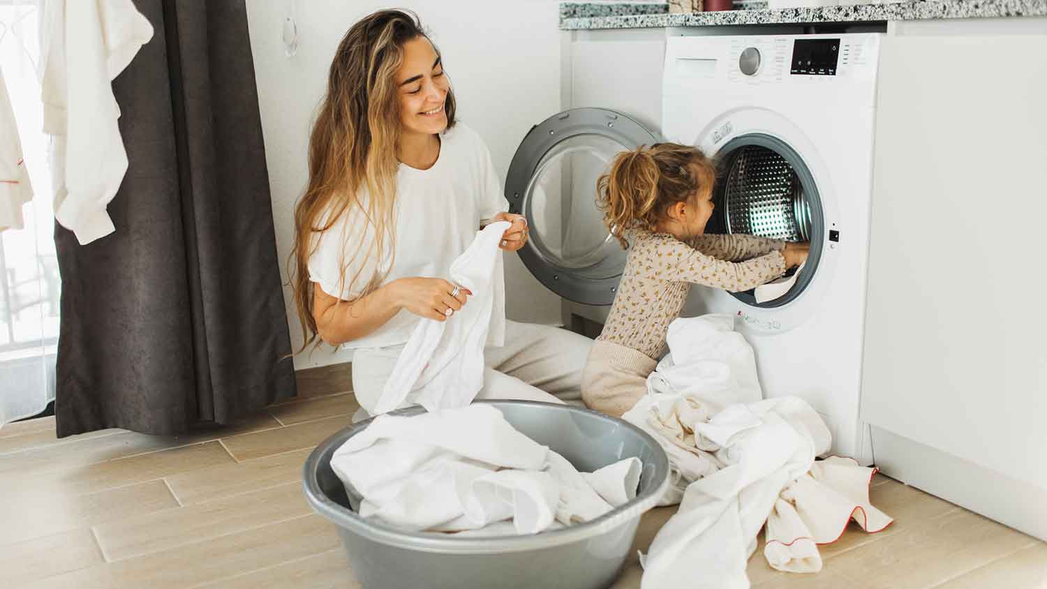 Mother and toddler daughter loading washing machine