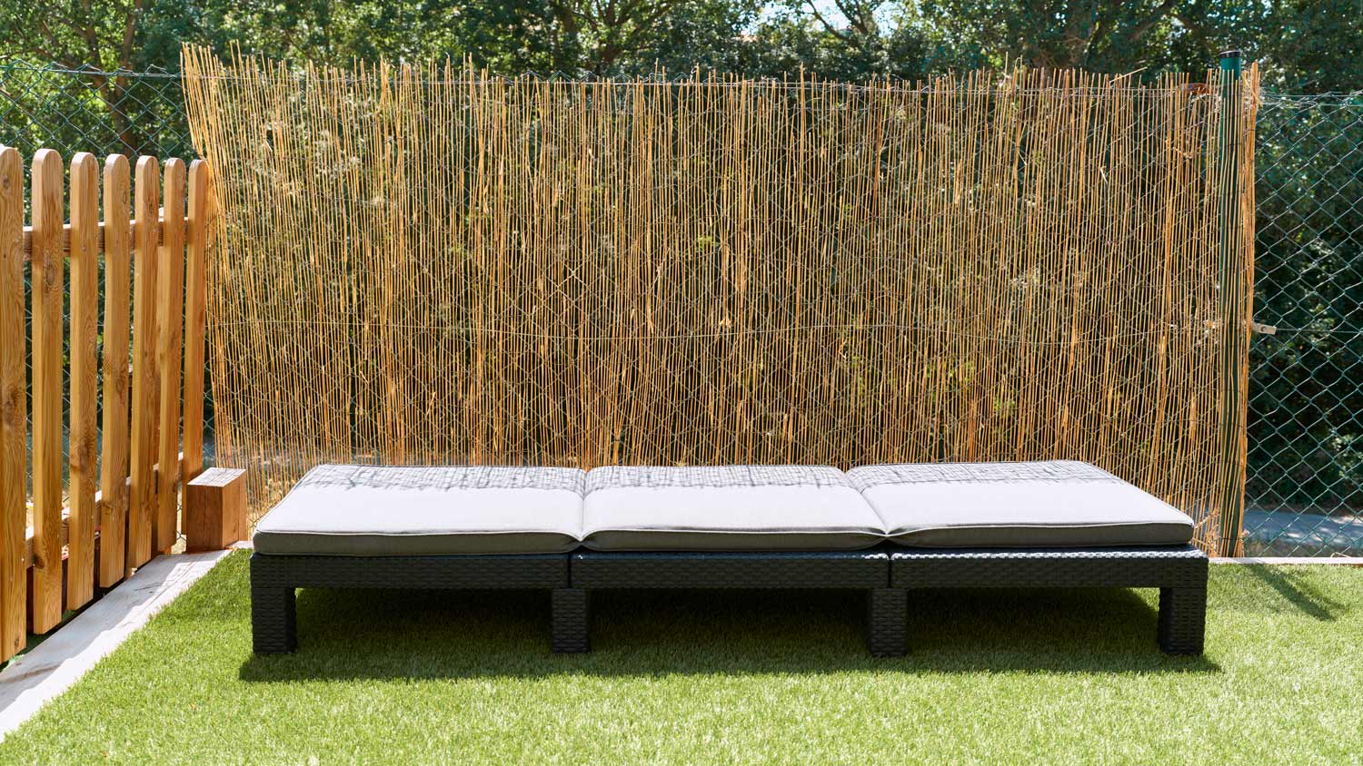 Front view of backyard with empty lounge chair in front of wooden fence
