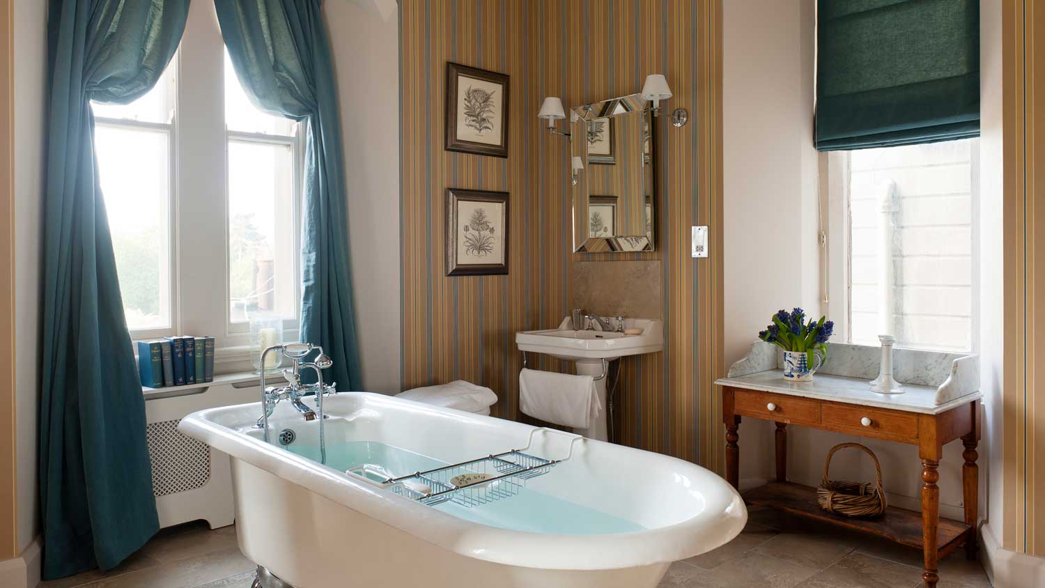 A free standing bathtub and stripped wallpaper in a cozy bathroom