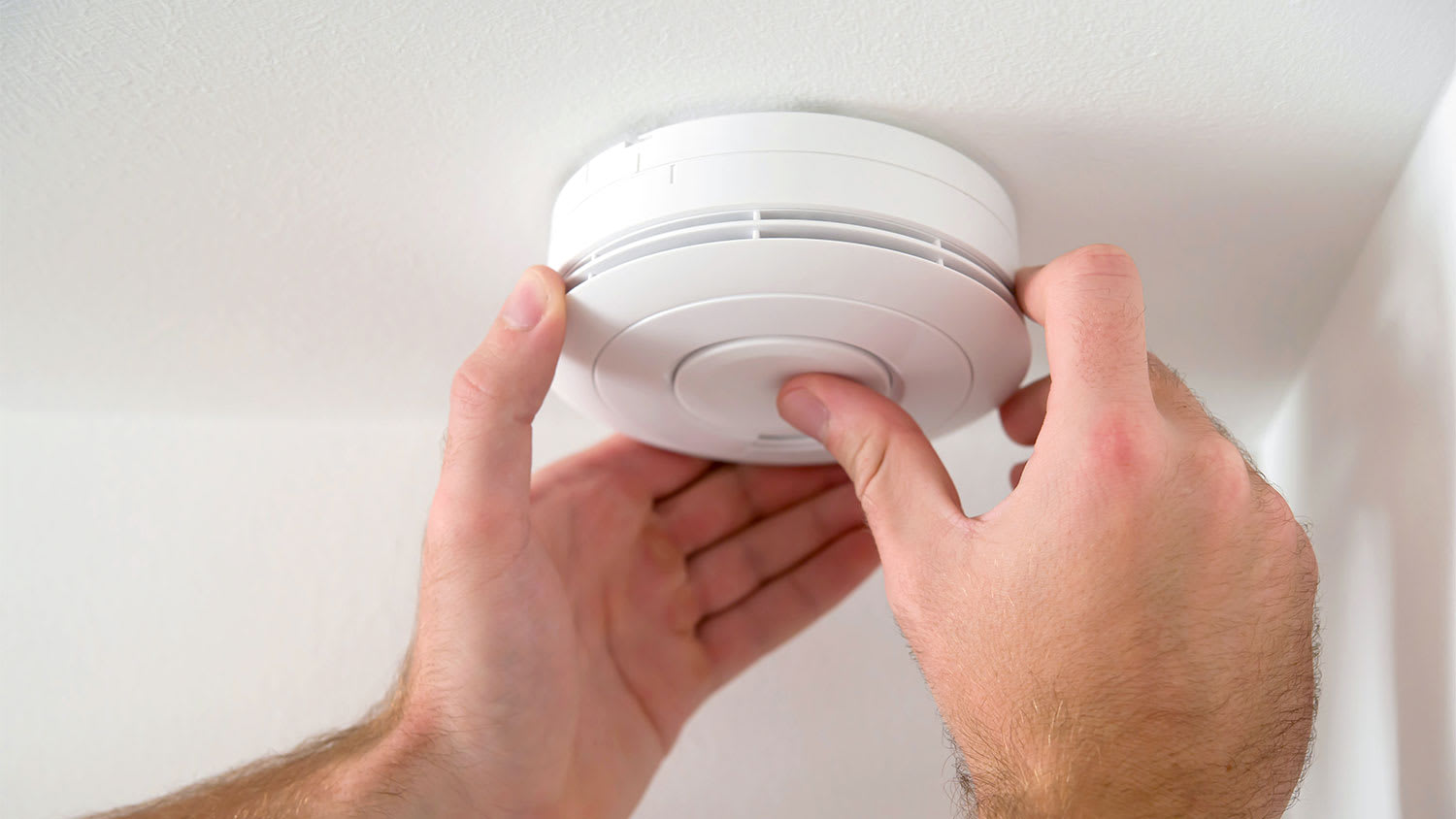 A view of a smoke detector reset button being pressed