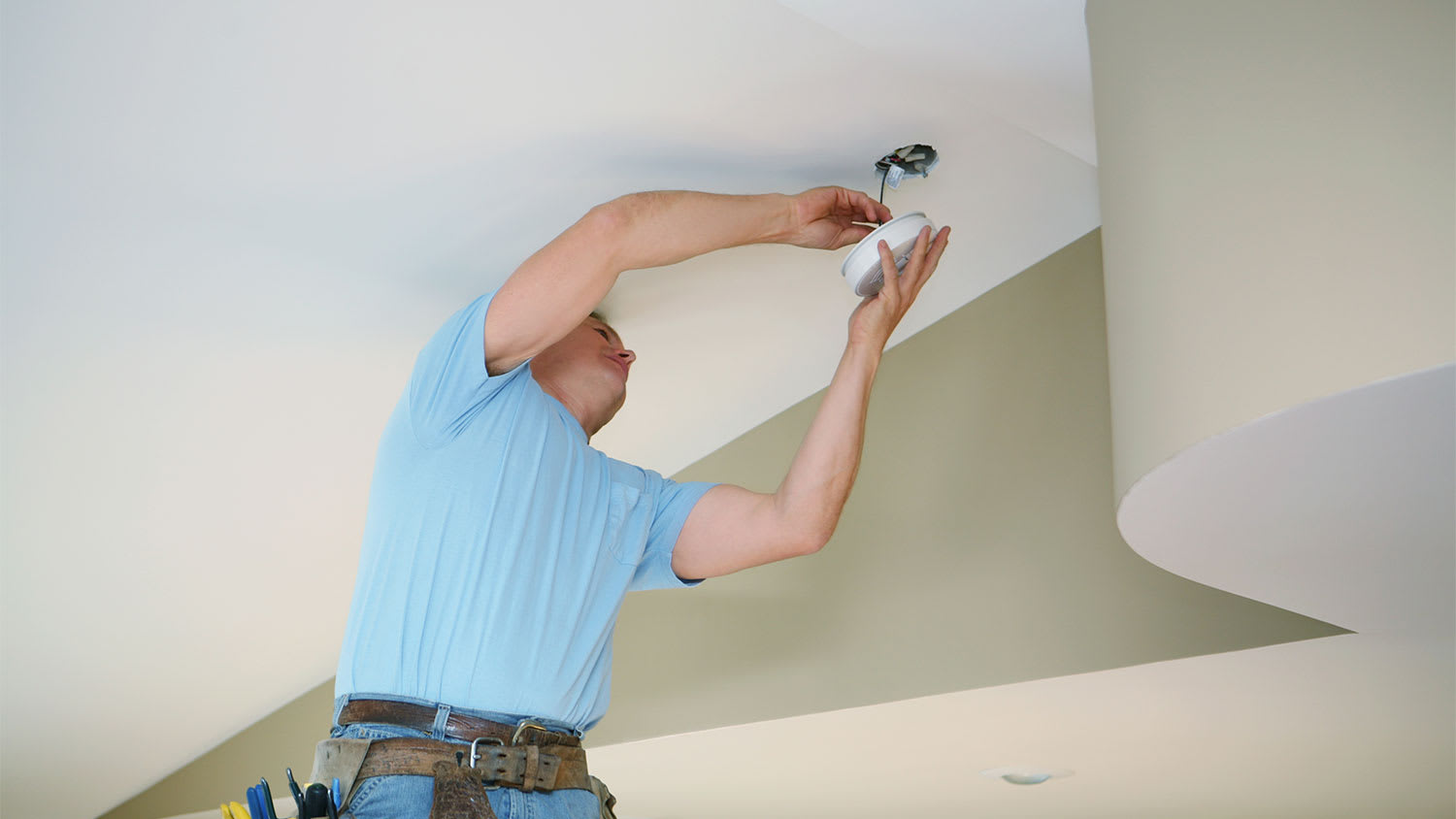 An electrician fixes a smoke detector