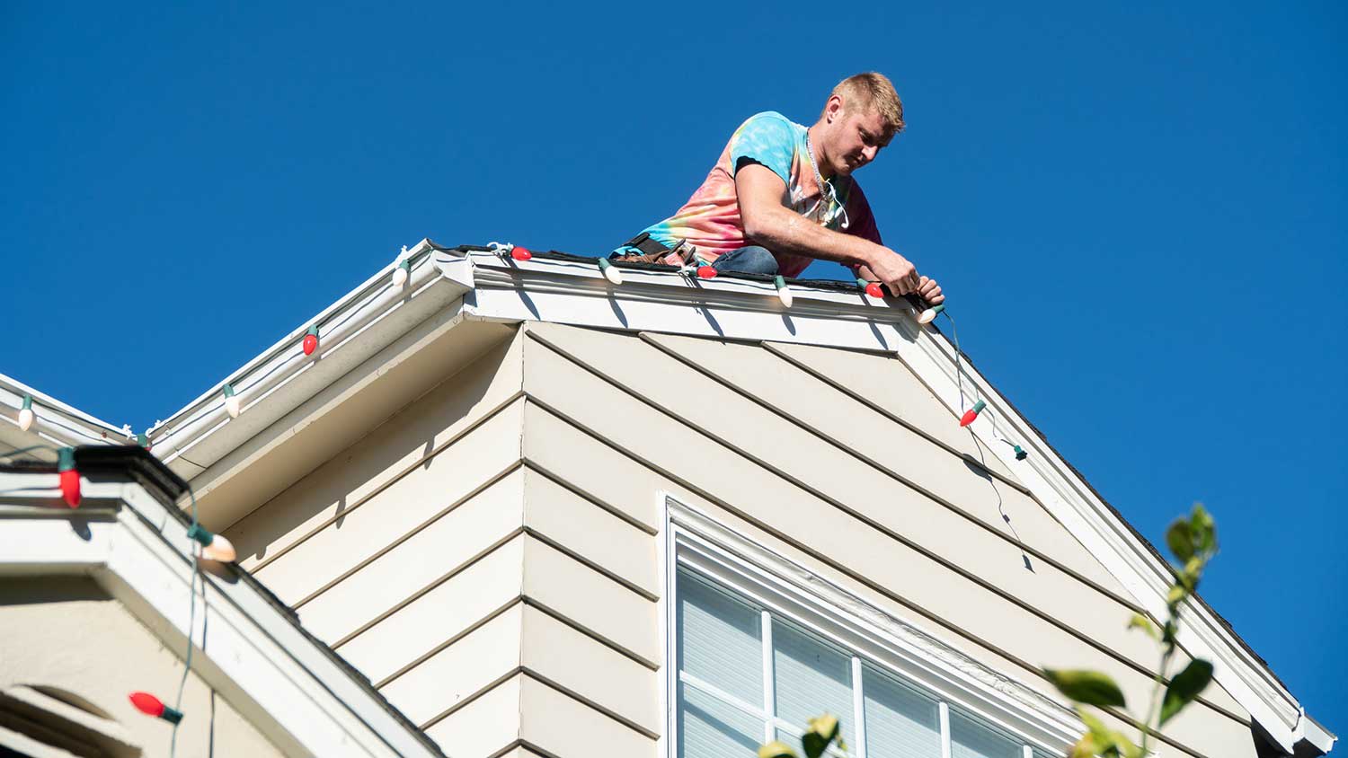 Handyman installing Christmas lights on a house roof