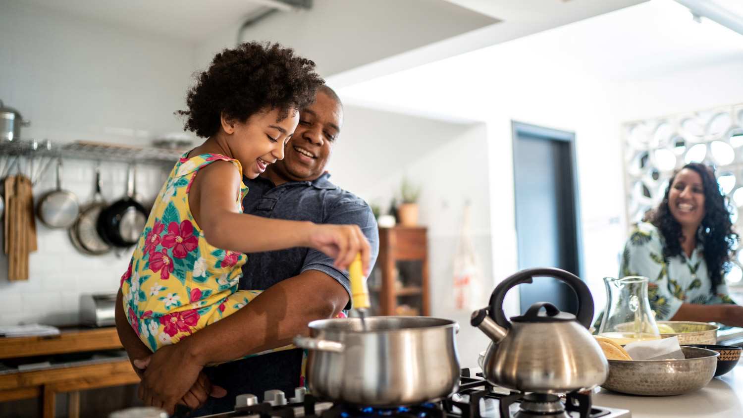Girl in father's arms helping him cooking at home