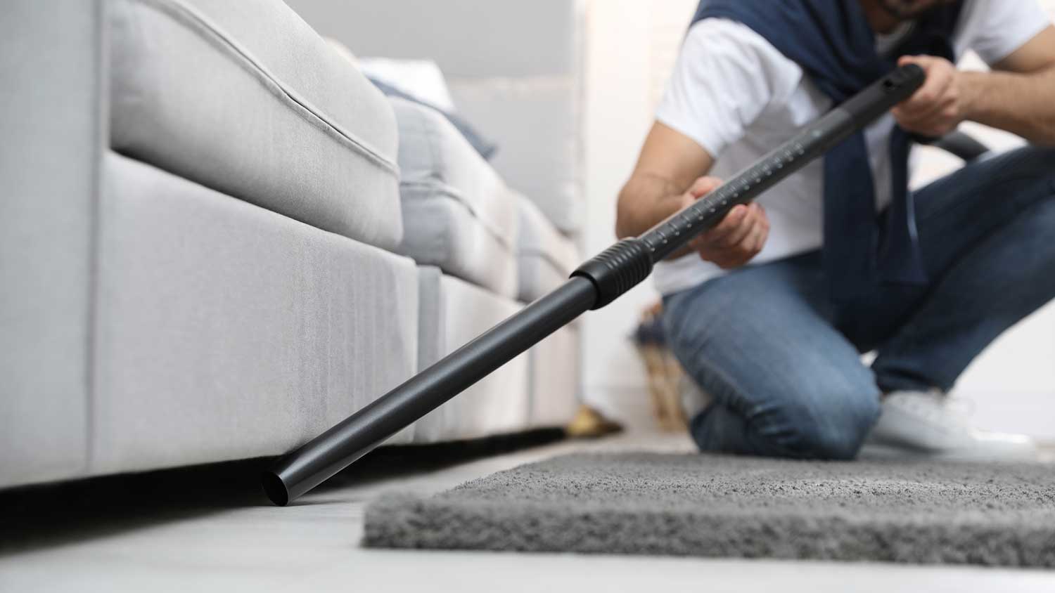 Man using vacuum cleaner to clean under the couch