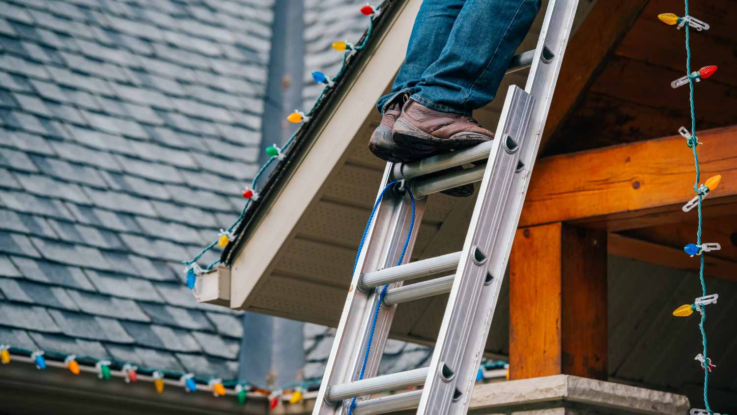 Man climbing ladder to hang up Christmas lights.