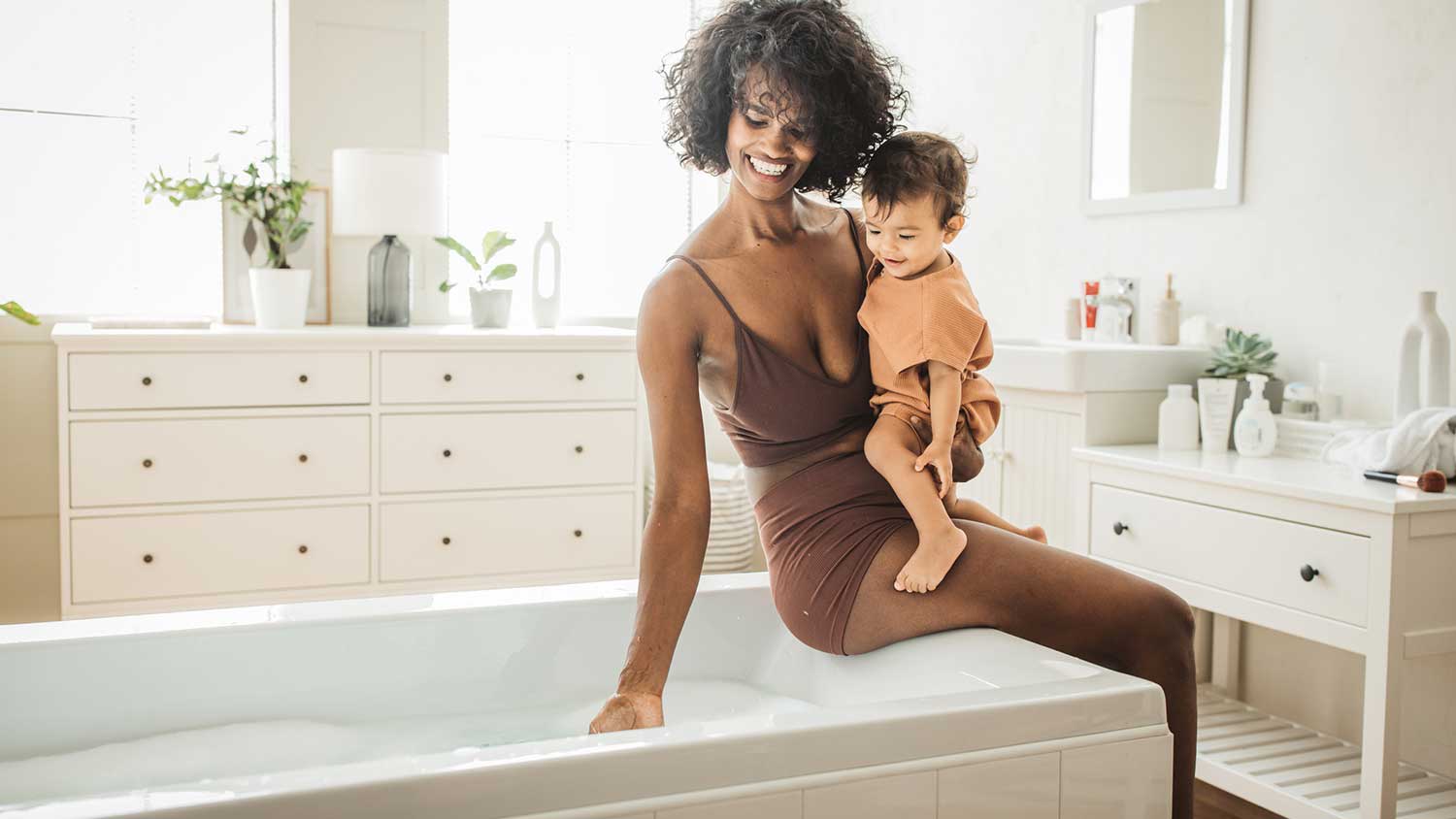Woman holding child is filling up the bathtub