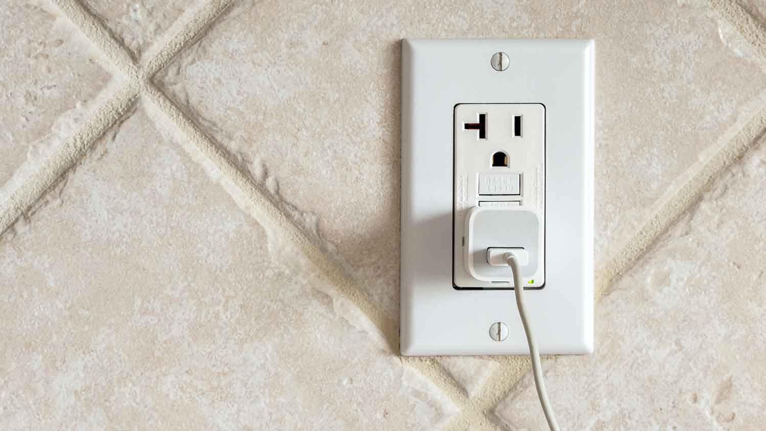 Charger plugged into GFCI outlet installed on a tile wall